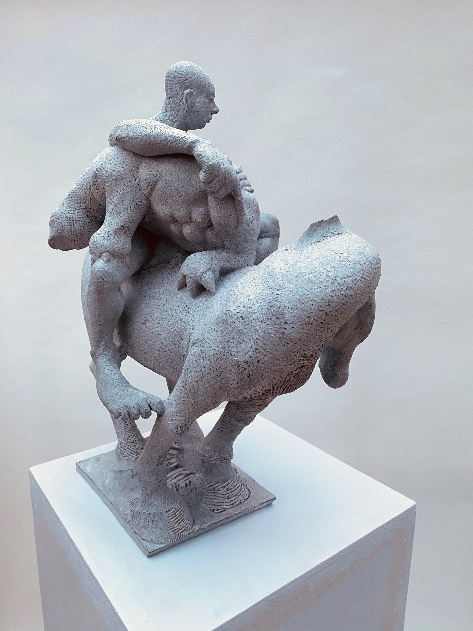 Sculpture made of grey fliedstone showing a human carrying an creature on a horse. 